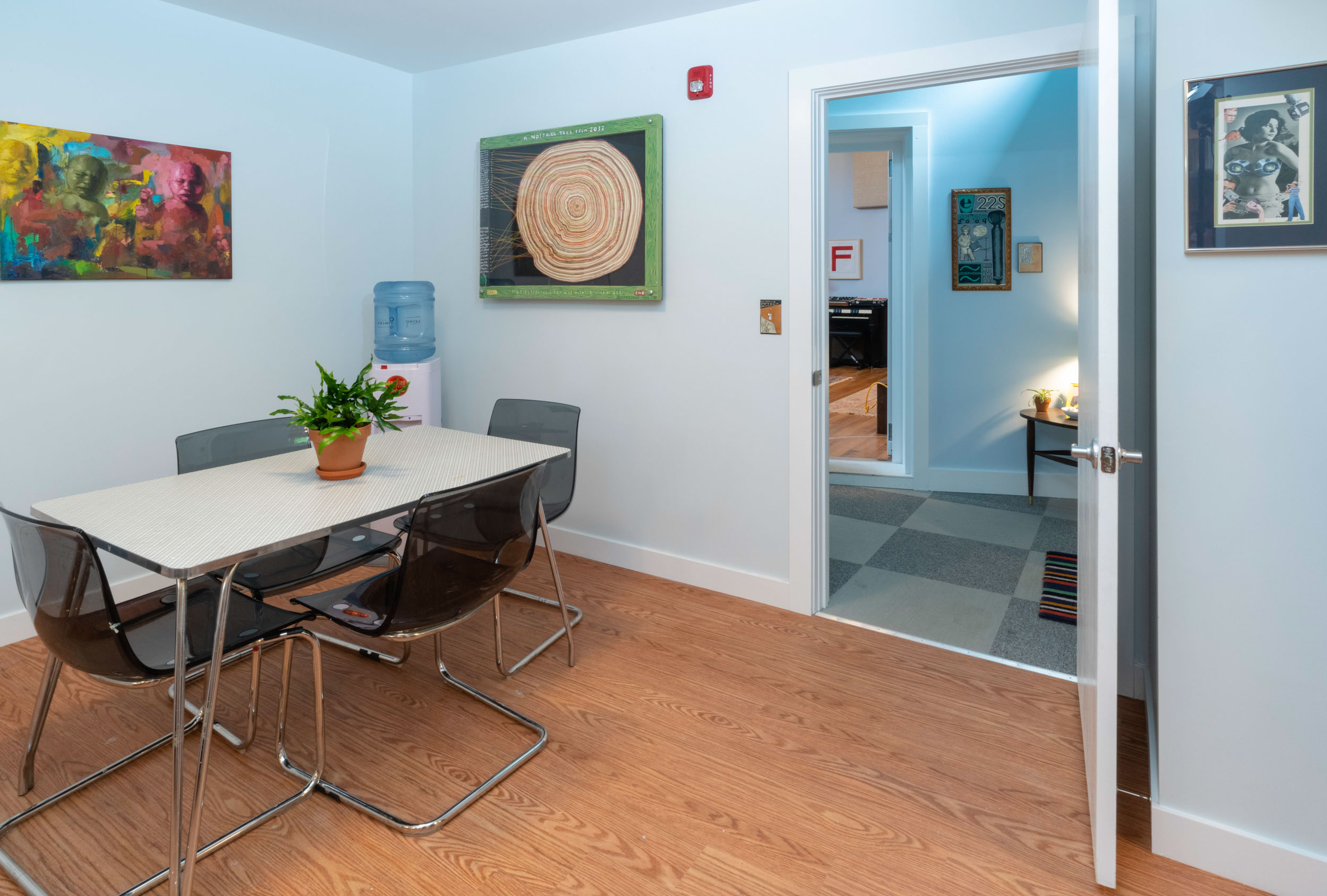 Dining room with table, four chairs, and colorful wall art under bright lighting.